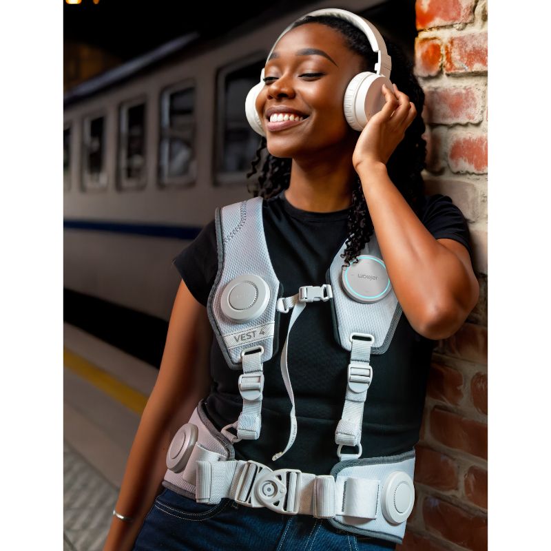 Woman smiling as she listens to music on headphones while wearing the white Woojer Vest 4 haptic vest, feeling every beat as vibroacoustic sensation