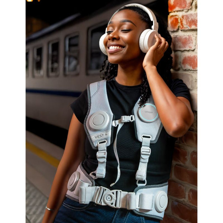 Woman smiling as she listens to music on headphones while wearing the white Woojer Vest 4 haptic vest, feeling every beat as vibroacoustic sensation
