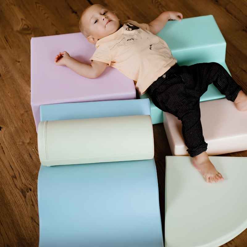 Baby lying across the foam shapes of the IGLU Explorer Soft Play Set in a pastel colourway