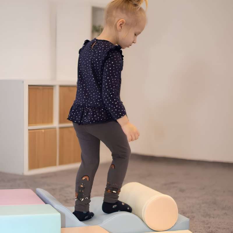 Toddler girl balancing on the foam cylinder of the IGLU Explorer Soft Play Set, building vestibular skills