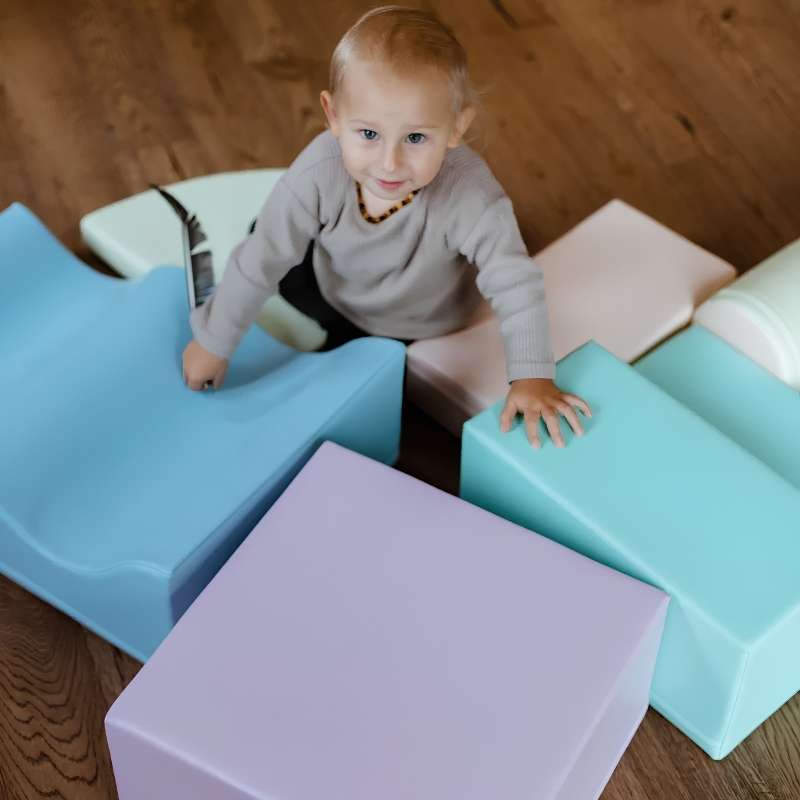 Toddler boy reaching for the wave shape on the IGLU Explorer Soft Play Set in a pastel colourway