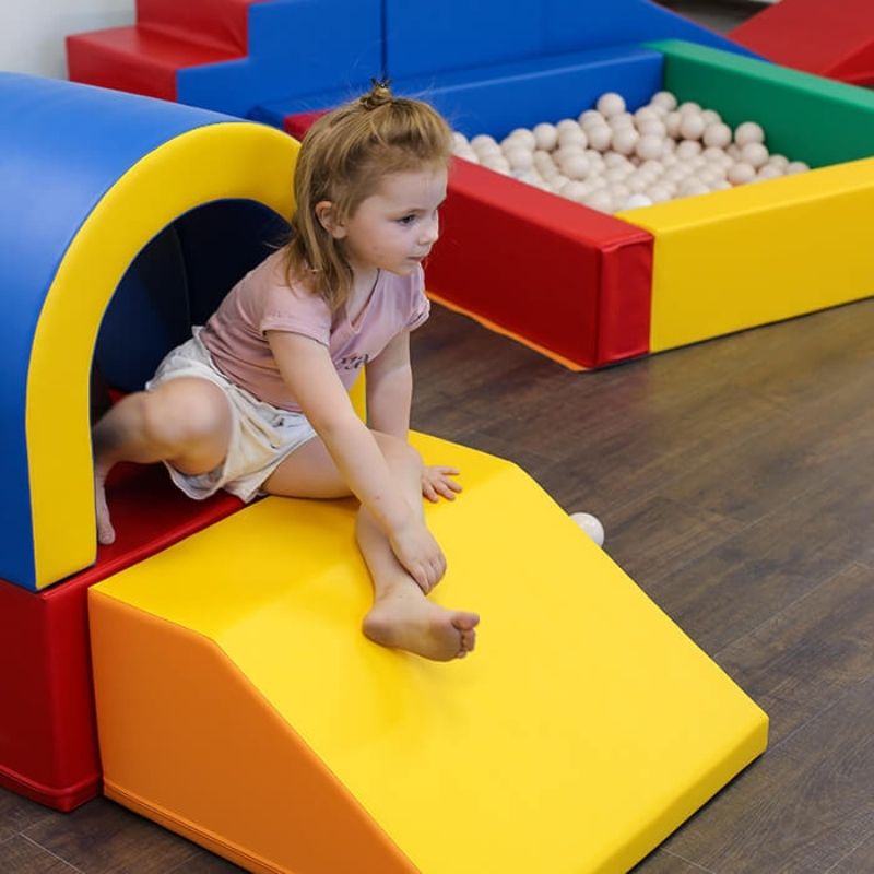 Child playing with the IGLU Imagination Tunnel soft play set, exploring and building imaginative play scenarios with modular foam shapes