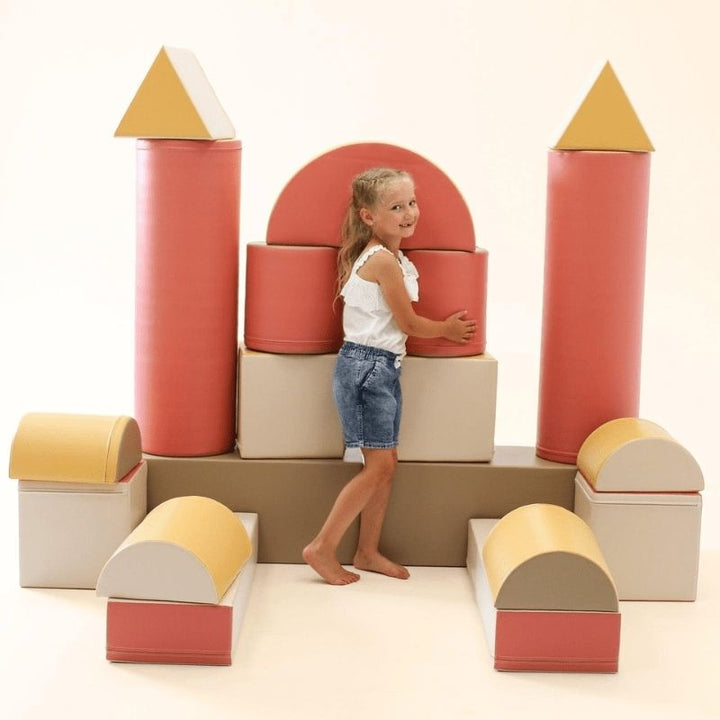 Girl playing castle with the IGLU Soft Play Fortress Set in pastel pink, using foam building blocks to create imaginative structures in a home setting