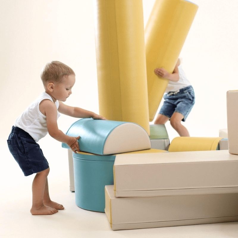 Boy climbing the IGLU Soft Play Fortress foam blocks in pastel turquoise, building coordination and gross motor skills through active indoor play