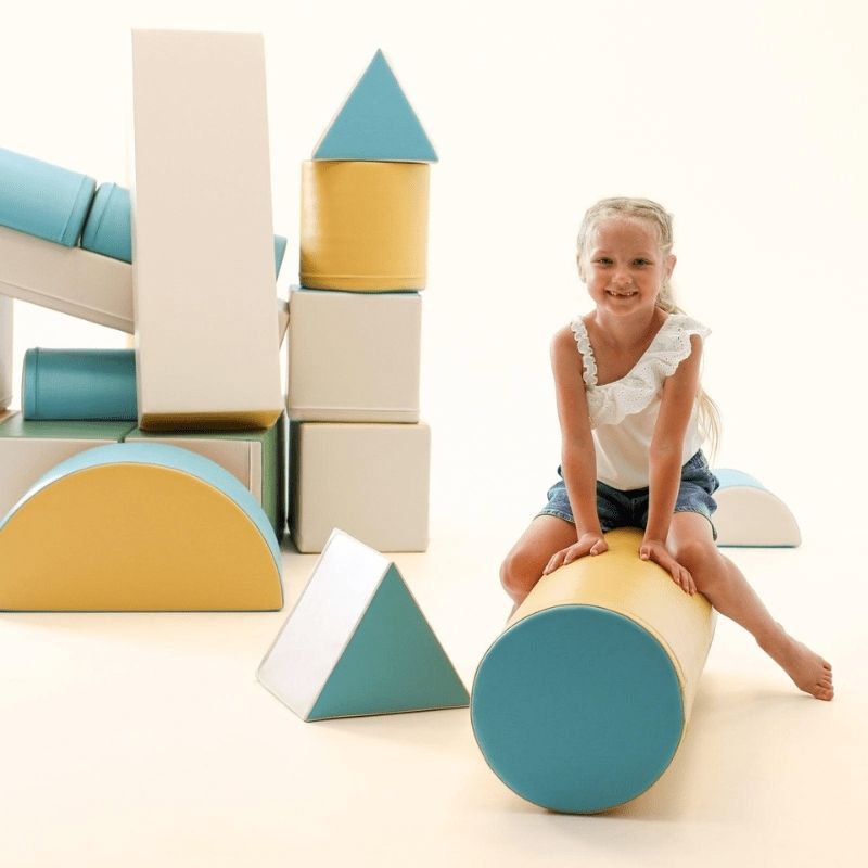 Child seated on the IGLU Soft Play Fortress foam blocks in pastel turquoise, showing the weight-bearing durability and safe surface for rest and play