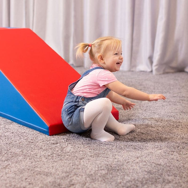 Child actively playing on IGLU Soft Play Mega Fun Slider in Red/Blue, showing foam climbing set for indoor gross motor play