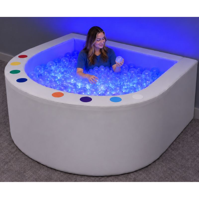 Adult sitting in the Experia Interactive LED Ball Pool holding a clear ball, surrounded by blue light in this illuminated sensory ball pit