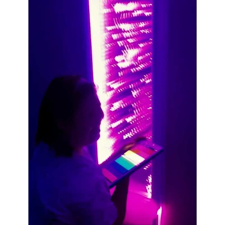A caregiver selects a colour on the MSE Genie controller in front of the pink lit TFH Infinity Bubble Wall, an interactive sensory bubble wall