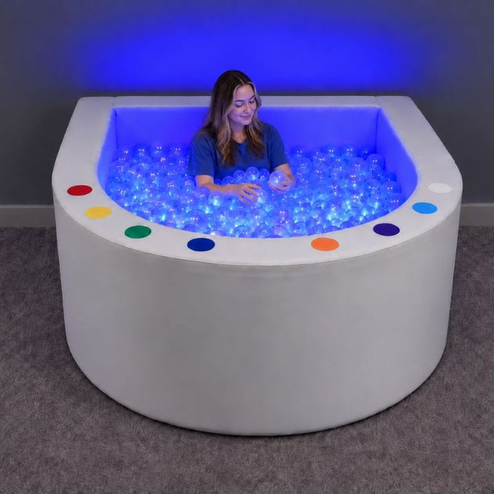 Adult relaxing among glowing clear balls in the Experia Interactive LED Ball Pool, an illuminated ball pool for all ages