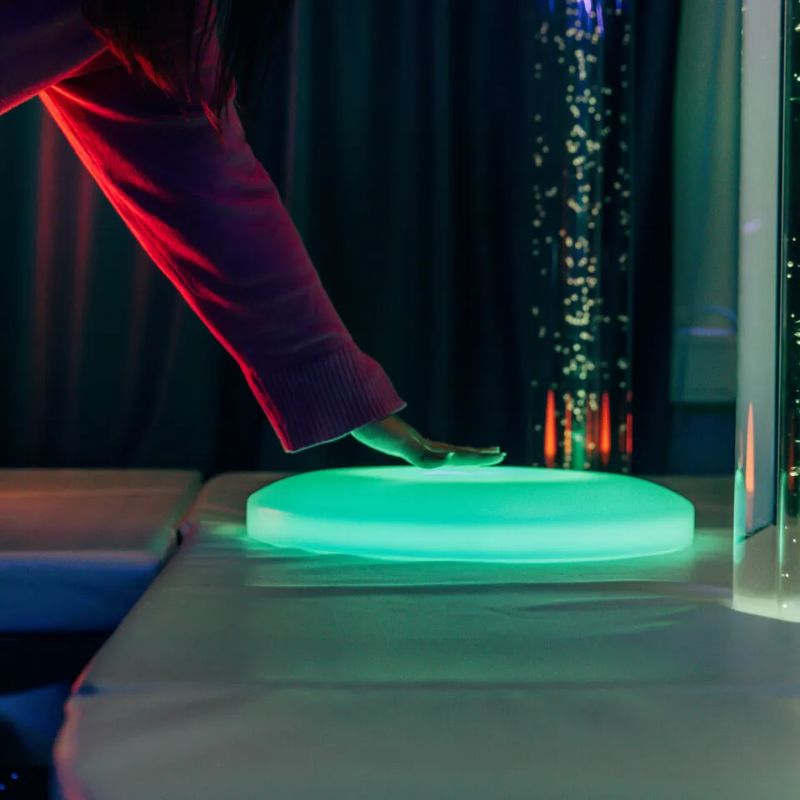 Hand touching the green TFH Illuminated Floor Splot on soft padded flooring, a light-up sensory floor tile for visual exploration and calm