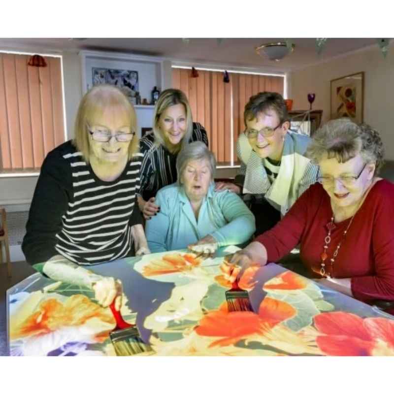 Older adults engaging with a Budii interactive sensory projector table activity, a reminiscence-themed painting game for senior care