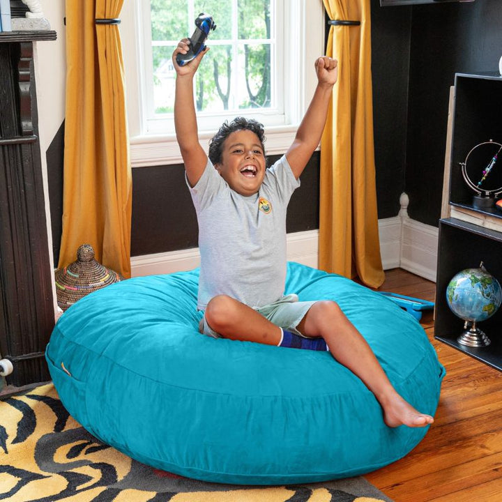 A boy celebrating a video game win on an aqua Jaxx Cocoon 4ft kids bean bag chair, a fun sensory crash pad