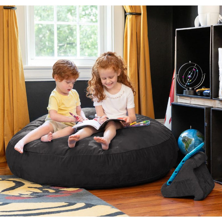 Two children reading together on a black Jaxx Cocoon 4ft kids bean bag chair, a versatile sensory crash pad