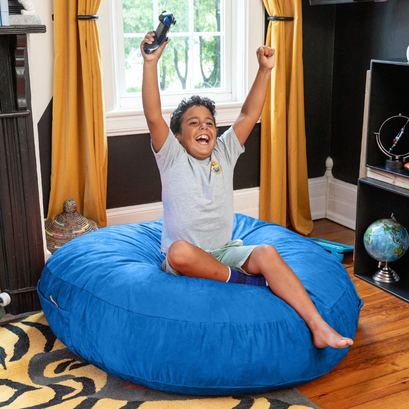 A boy celebrating a video game win on a blue Jaxx Cocoon 4ft kids bean bag chair, a cozy deep pressure seat