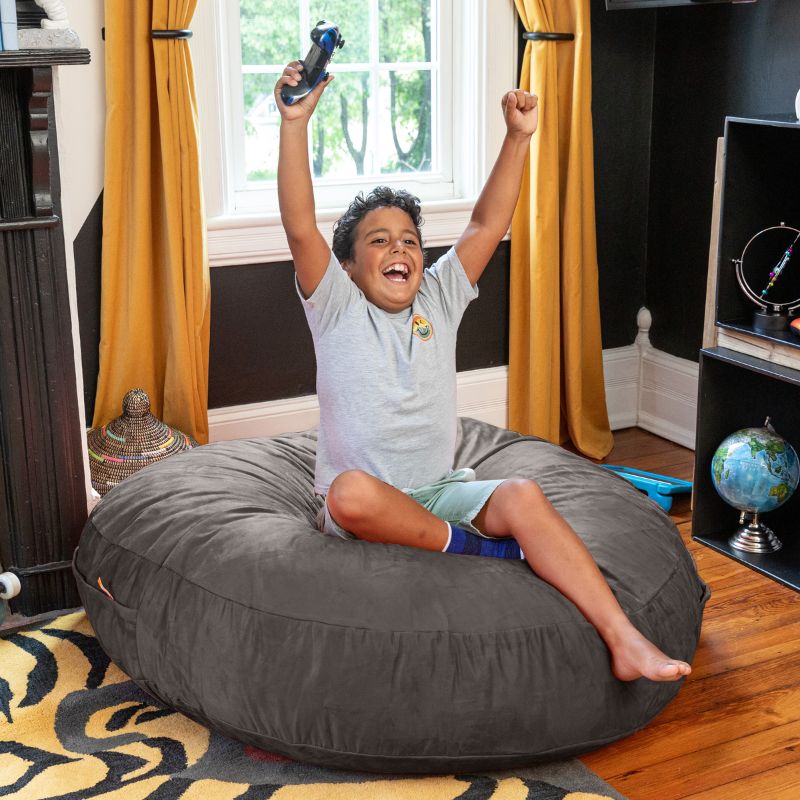 A boy celebrating a video game win on a dark gray Jaxx Cocoon 4ft kids bean bag chair, a supportive sensory seat