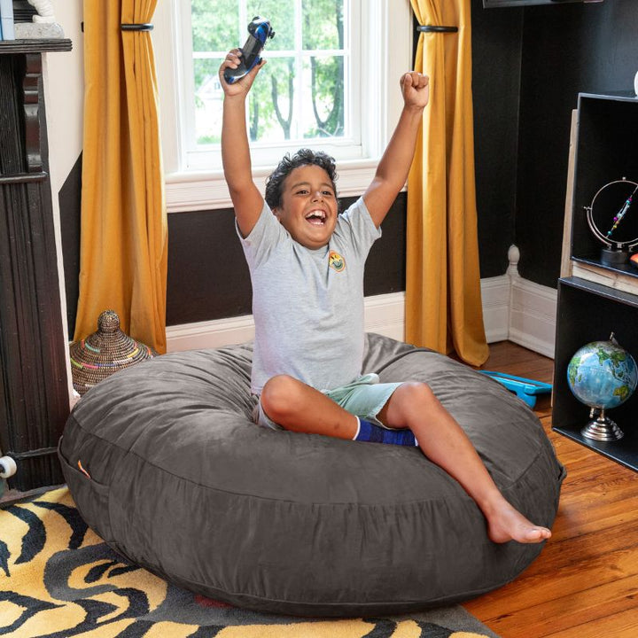 A boy celebrating a video game win on a dark gray Jaxx Cocoon 4ft kids bean bag chair, a supportive sensory seat
