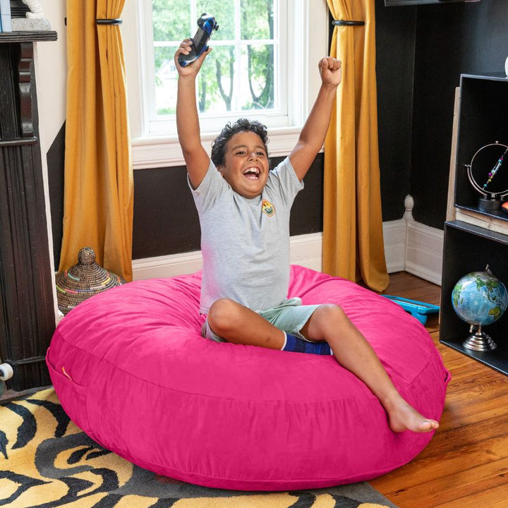 A boy celebrating a video game win on a fuchsia Jaxx Cocoon 4ft kids bean bag chair, a bright sensory seat