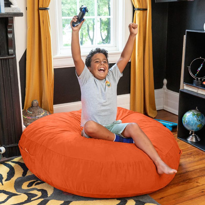A boy celebrating a video game win on an orange Jaxx Cocoon 4ft kids bean bag chair, a vibrant sensory seat