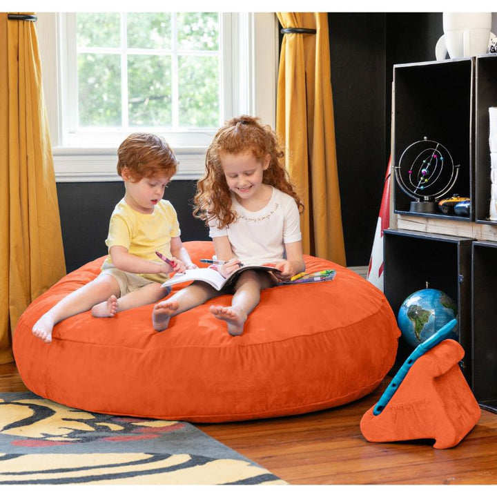 Two children reading together on an orange Jaxx Cocoon 4ft kids bean bag chair, a vibrant sensory crash pad