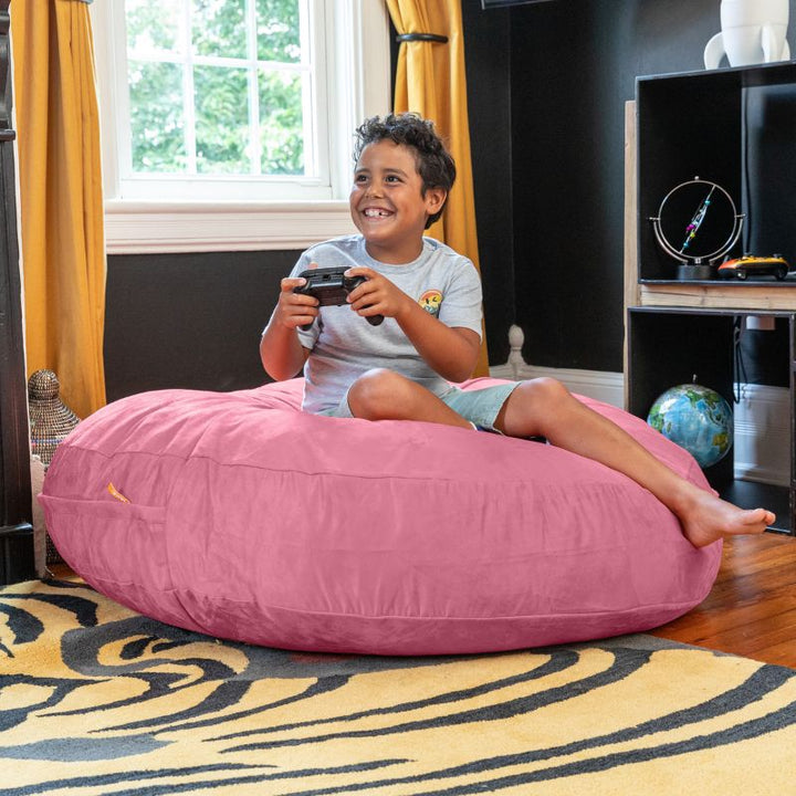 A boy playing video games on a pink Jaxx Cocoon 4ft kids bean bag chair, a soft sensory crash pad