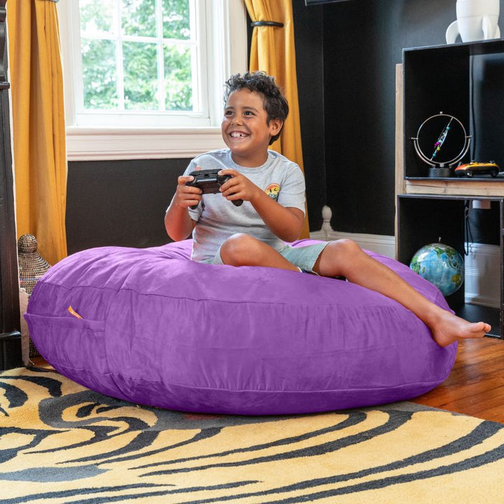 A boy celebrating a video game win on a purple Jaxx Cocoon 4ft kids bean bag chair, a calming sensory seat