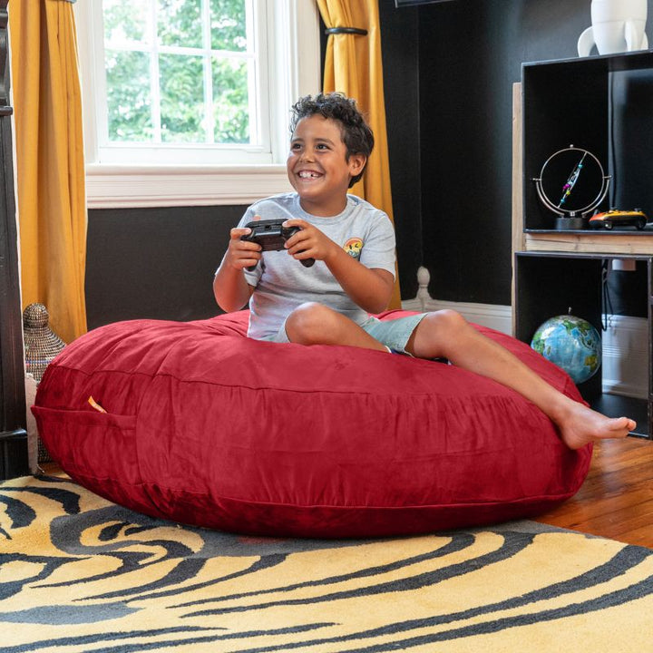 A boy playing video games on a red Jaxx Cocoon 4ft kids bean bag chair, a bold sensory crash pad