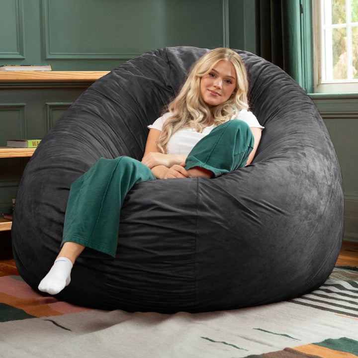A woman relaxing in a black Jaxx Cocoon 6ft bean bag chair, an oversized sensory seat