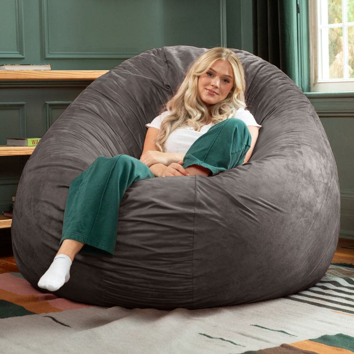 A woman relaxing in a charcoal Jaxx Cocoon 6ft bean bag chair, a supportive oversized sensory seat