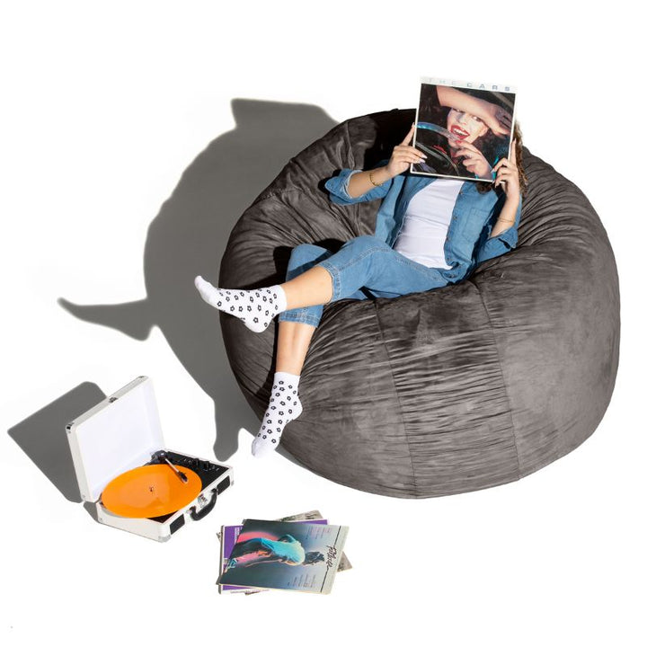 A woman relaxing with records on a charcoal Jaxx Cocoon 6ft bean bag chair, an oversized sensory lounger