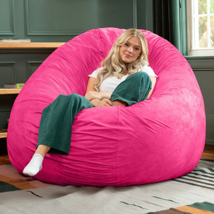 A woman relaxing in a fuchsia Jaxx Cocoon 6ft bean bag chair, a bright giant sensory lounger