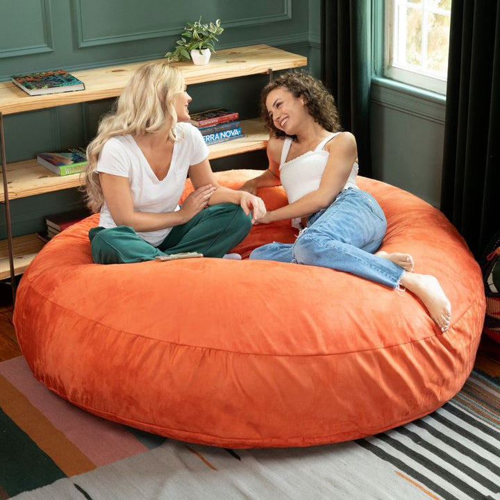 Two friends sitting together on an mandarin Jaxx Cocoon 6ft bean bag chair, a vibrant sensory seat