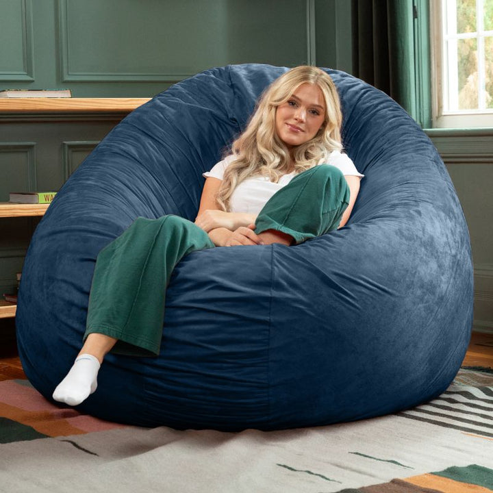 A woman relaxing in a navy Jaxx Cocoon 6ft bean bag chair, a calming oversized sensory lounger