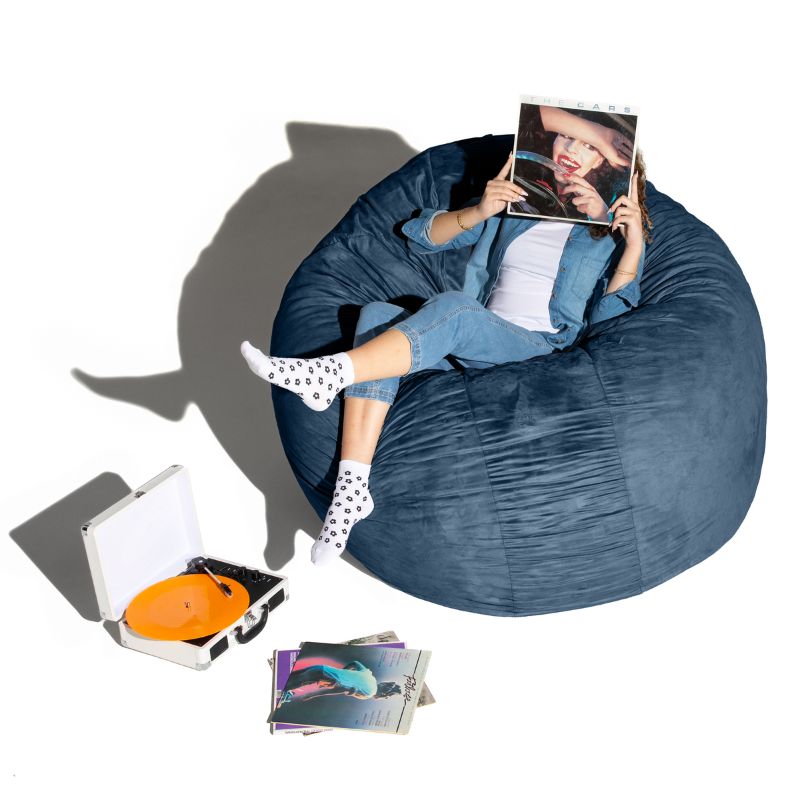 A woman relaxing with records on a navy Jaxx Cocoon 6ft bean bag chair, a calming oversized sensory lounger