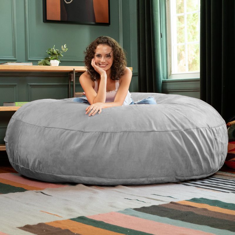 A woman lounging on a platinum Jaxx Cocoon 6ft bean bag chair, a neutral giant sensory seat
