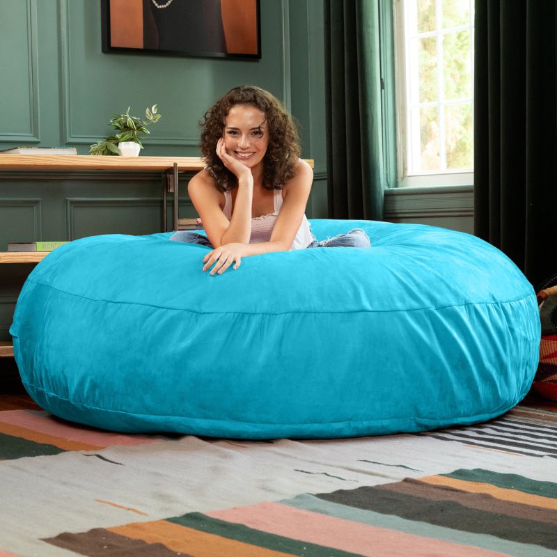 A woman lounging on a turquoise Jaxx Cocoon 6ft bean bag chair, a cool-toned oversized sensory lounger