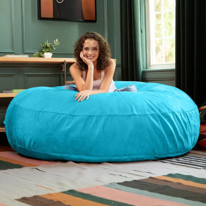 A woman lounging on a turquoise Jaxx Cocoon 6ft bean bag chair, a cool-toned oversized sensory lounger