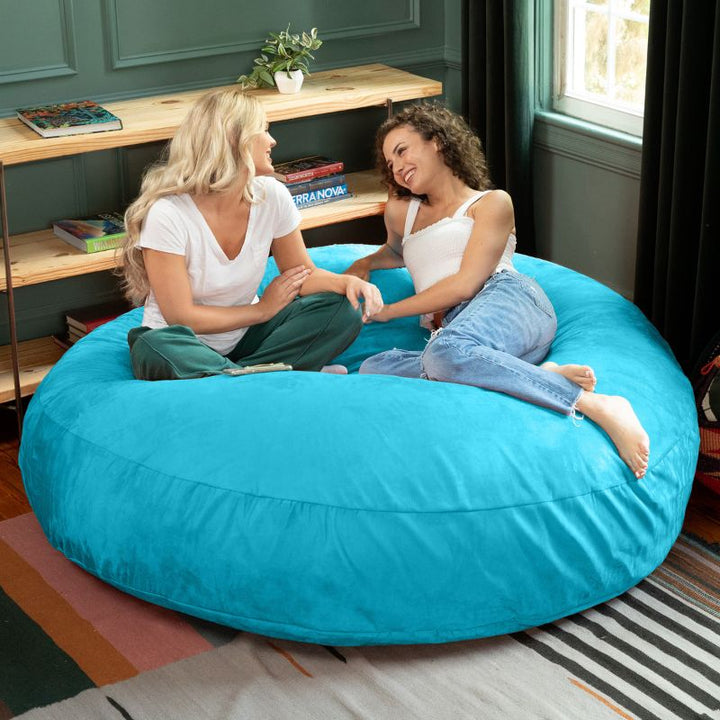 Two friends sitting together on a turquoise Jaxx Cocoon 6ft bean bag chair, a cool-toned sensory lounger