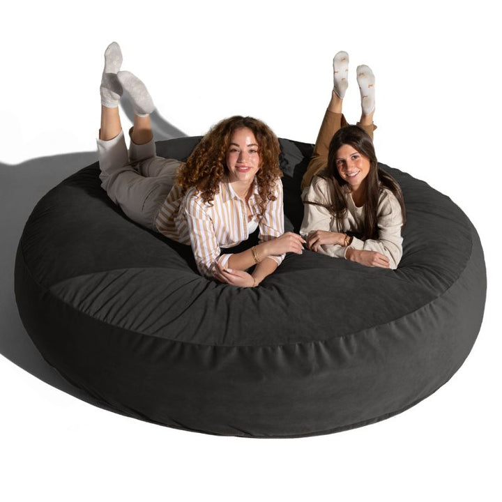 Two friends lounging on a black Jaxx Cocoon 7ft XL bean bag chair, the largest sensory crash pad and lounger