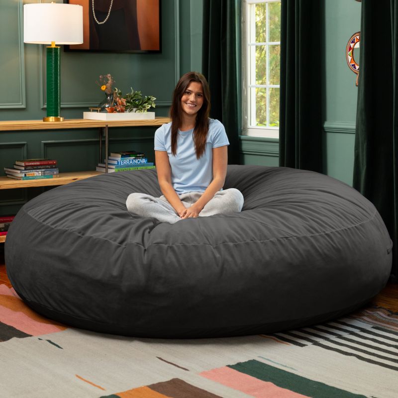 A woman sitting cross-legged on a black Jaxx Cocoon 7ft XL bean bag chair, the largest sensory lounger