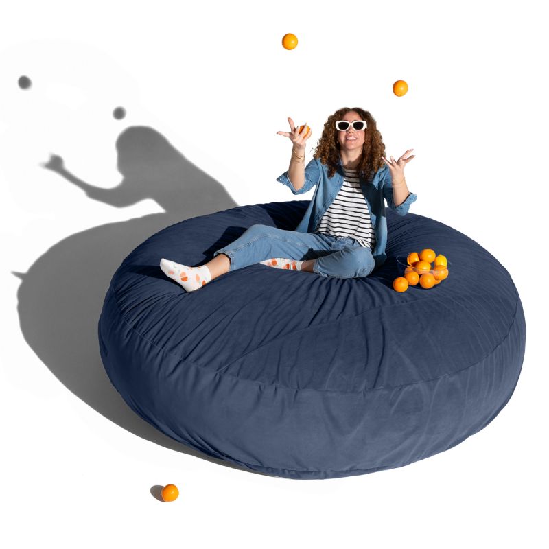 A woman relaxing on a blue Jaxx Cocoon 7ft XL bean bag chair, a calming oversized sensory seat