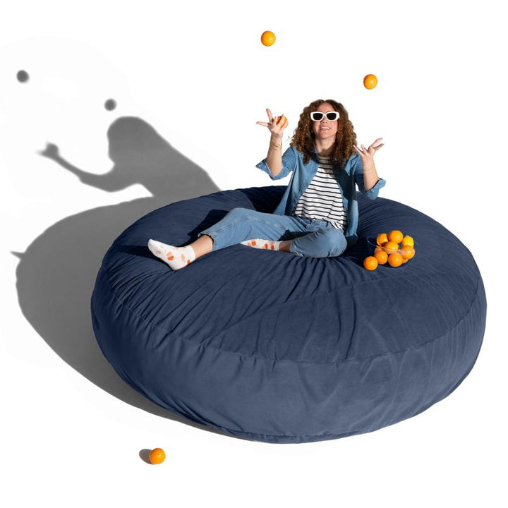 A woman relaxing on a blue Jaxx Cocoon 7ft XL bean bag chair, a calming oversized sensory seat
