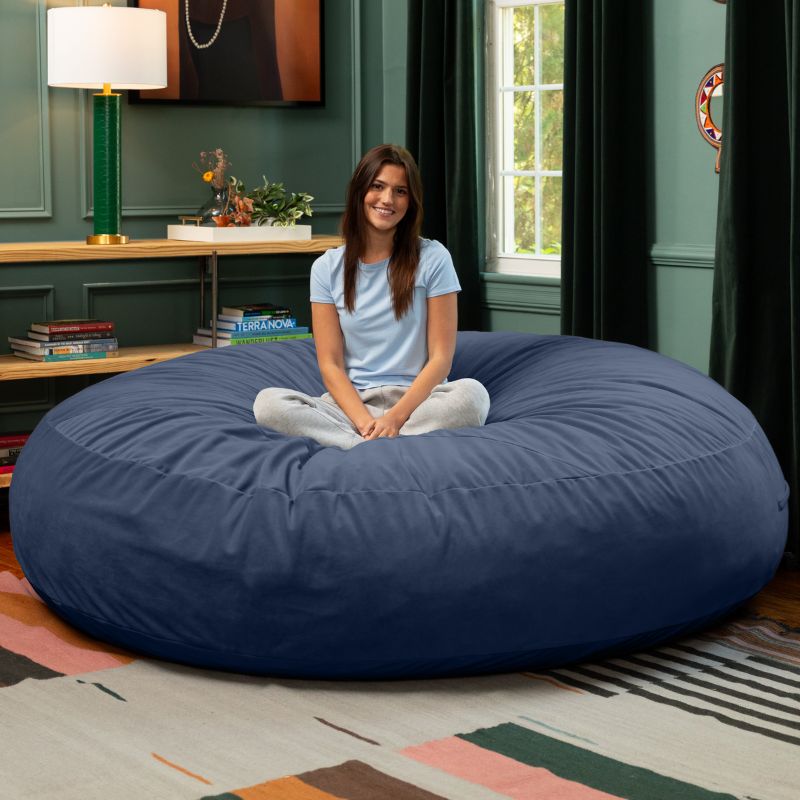 A woman sitting cross-legged on a blue Jaxx Cocoon 7ft XL bean bag chair, a calming oversized lounger