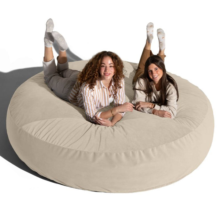 Two friends lounging on a cream Jaxx Cocoon 7ft XL bean bag chair, a soft oversized deep pressure seat