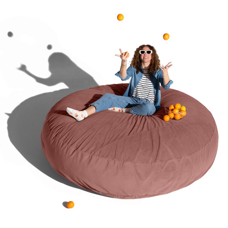 A woman relaxing on a mauve Jaxx Cocoon 7ft XL bean bag chair, an extra-large sensory crash pad