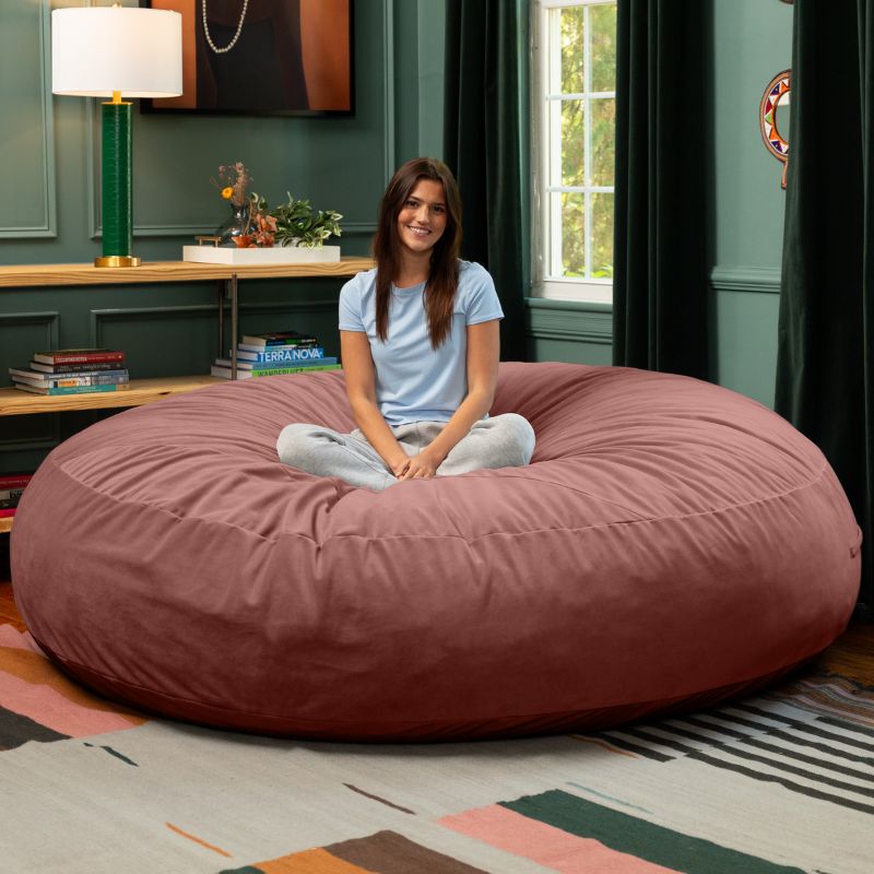 A woman sitting cross-legged on a mauve Jaxx Cocoon 7ft XL bean bag chair, an extra-large sensory lounger