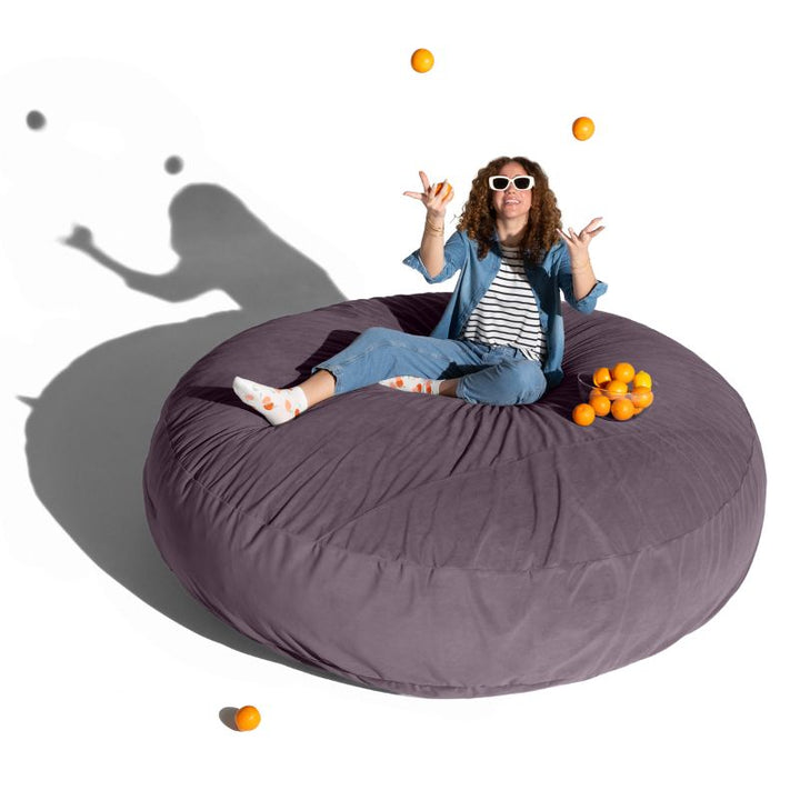 A woman relaxing on a purple Jaxx Cocoon 7ft XL bean bag chair, an extra-large sensory crash pad