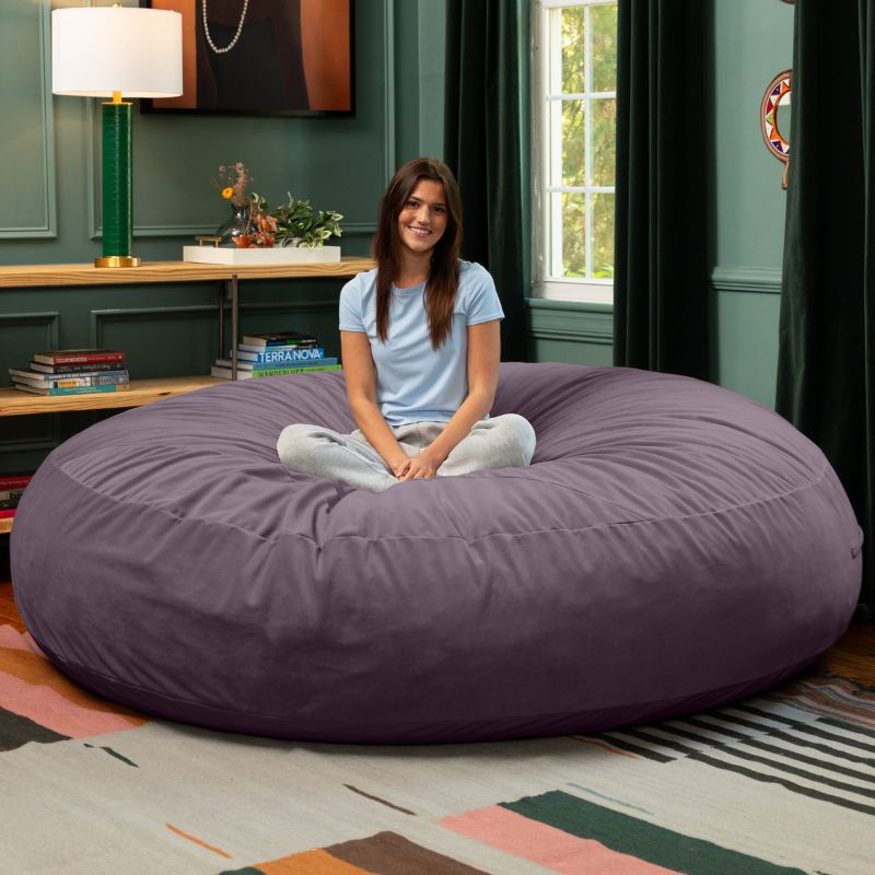 A woman sitting cross-legged on a purple Jaxx Cocoon 7ft XL bean bag chair, an extra-large sensory seat