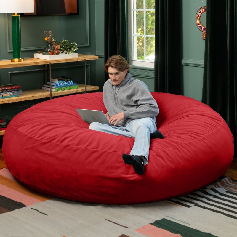 A man working on a laptop on a red Jaxx Cocoon 7ft XL bean bag chair, a bold giant sensory seat