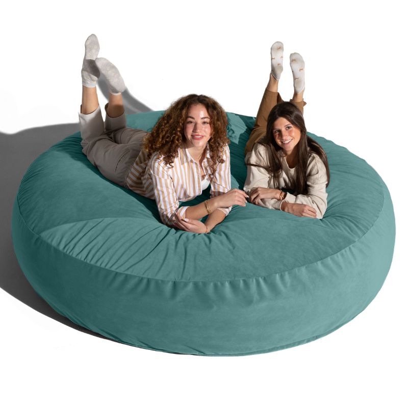 Two friends lounging on a turquoise Jaxx Cocoon 7ft XL bean bag chair, the largest sensory lounger