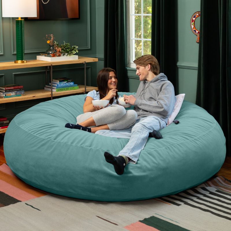 Two friends sharing snacks on a turquoise Jaxx Cocoon 7ft XL bean bag chair, the largest sensory lounger